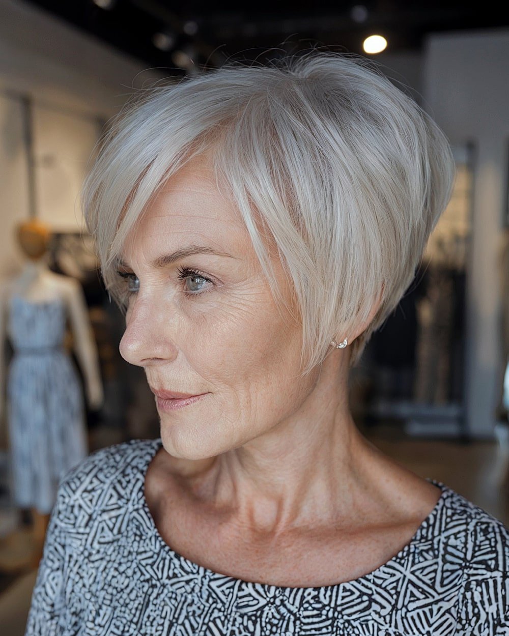 Angled micro bob haircut for women over 60 with fine white-blonde hair and sleek side-swept fringe