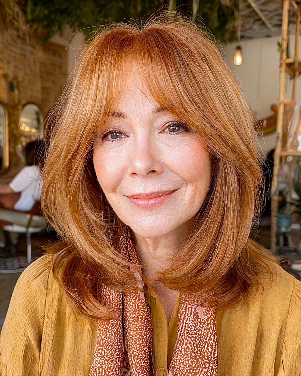 Shoulder length strawberry blonde hair with curtain bangs and light texture for women in their 60s