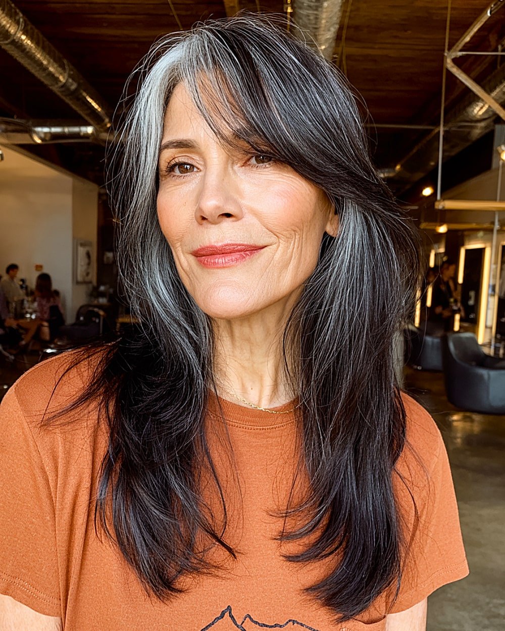 Long dark layered hair with silver streaks and side bangs for older women